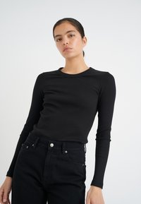Svart randig långärmad topp med rund halsringning, kombinerad med högmidjade svarta jeans. Slätt tyg och figurnära design.