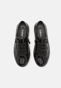Scarpe in vernice nera con lacci frontali e chiusura laterale con zip, dotate di una soletta testurizzata e suola in gomma rigata. Nome del marchio visibile all'interno.