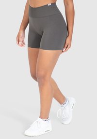 Hooggewaisted, slim-fitting shorts in donkergrijs, gemaakt van een gladde stof met een rekbare tailleband. Gecombineerd met witte sneakers en enkelsokken.
