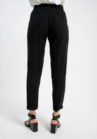 Czarne zwężane spodnie z elastycznym paskiem w talii, z podwiniętymi mankietami i gładką fakturą. Noszone z sandałami na wysokim obcasie.