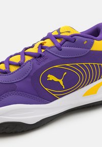 Puma Sportschuh mit einem lila Mesh-Obermaterial, gelben Akzenten und strukturierten synthetischen Überzügen. Verfügt über ein schwarzes Logo und eine kontrastierende weiße Sohle.
