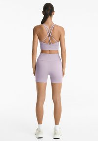 Lilac urheiluliivit, joissa on ristiselän hihnat, yhdistetty korkeavyötäröisiin lilac-shortsihin. Sujuva kangas, jossa on minimaalinen brändäys. Urheilullinen tyyli.