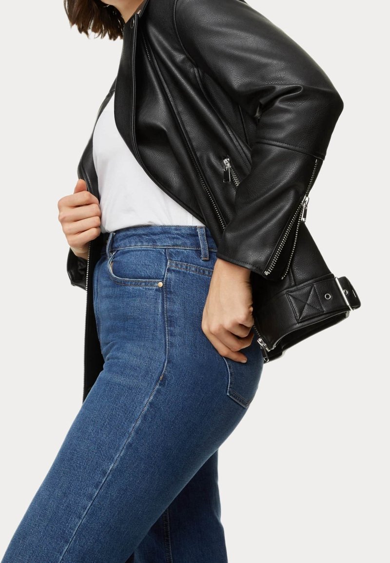 Svart läderjacka med metallisk dragkedja, i kombination med mörkblå denimjeans. Jackan har en figursydd design och texturerade detaljer.