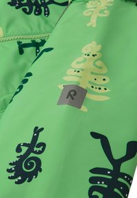 Tessuto di giacca impermeabile verde con un mix di motivi fogliari astratti in verde chiaro e scuro. Include una piccola etichetta logo grigia.