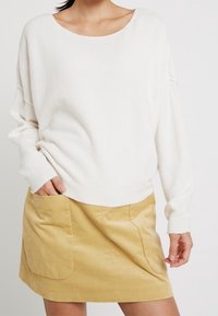 Vit oversized tröja med vid halsringning, kombinerad med en ljusbeige kordflorskjol med stora framfickor.