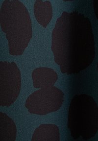 Dunkelgrüner Stoff mit großen, unregelmäßigen schwarzen Flecken. Die Textur wirkt weich und glatt und weist eine gemischte und leicht strukturierte Oberfläche auf.