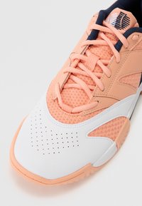 Sneaker med en kombinasjon av myk ferskenmesh og hvitt skinn, med perforeringer på tåen. Mørke marineblå aksenter på tungen og snøringene.