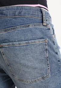 Pantalones vaqueros azules de mezclilla que muestran una vista de cerca de los bolsillos traseros, con detalles visibles de costuras y un tejido suave y texturizado.