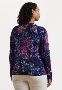 Tröja i marinblått med en färgglad blommönster som innehåller röda, gula och blå nyanser. Stickad textur med långa ärmar och ribbad nederkant.