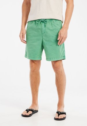 Groene katoenen zwemshorts met een elastische tailleband en drawstring, voorzien van zijzakken en een relaxte pasvorm, gecombineerd met zwarte teenslippers.