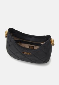 Czarna torebka pikowana, wykonana z teksturowanego materiału, z dodatkiem złotego zamka błyskawicznego i detalu logo wewnątrz. Kompaktowy kształt o zaokrąglonym profilu.