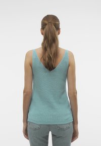 Een lichtblauw, mouwloos top met een V-uitsnijding op de rug, gemaakt van textuur gebreide stof. De zoom is recht en valt net onder de heupen.