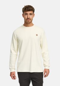 Helles gelbes Langarmshirt mit gerippter Textur, Rundhalsausschnitt und einem kleinen braunen runden Logo auf der linken Brust.