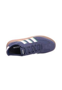 Navy blue Adidas sneaker with white stripes and green accents, brown rubber sole, and lace-up design viewed from above.