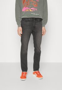 Slim-fit black jeans with a subtle faded texture, paired with a long-sleeve gray graphic sweatshirt and orange sneakers.