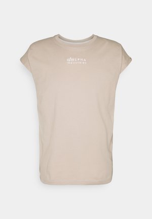 Beżowy bezrękawnik z okrągłym dekoltem oraz logo "Alpha Industries" umieszczonym na środku klatki piersiowej w białym kolorze.