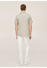 Světle šedá polo košile s krátkým rukávem a jemnou texturou, kombinovaná s bílými kalhotami a světlými teniskami. Jednoduchý, čistý design.