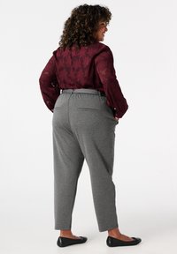 Bordeaux bloes met bloemenpatroon, grijze getailleerde broek met elastische tailleband, en zwarte platte schoenen gezien vanaf de achterkant.