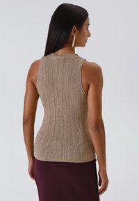 Mouwloze gebreide top in metallic beige. Kenmerken ribbelstructuur, hoge hals en een aansluitende sle silhouette, gecombineerd met een gelaagde bordeauxrode rok.