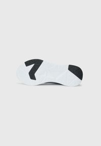 Semelle de baskets blanches avec des pastilles de grip en caoutchouc noir au talon et à l'orteil, motif de semelle géométrique, isolée sur fond clair.