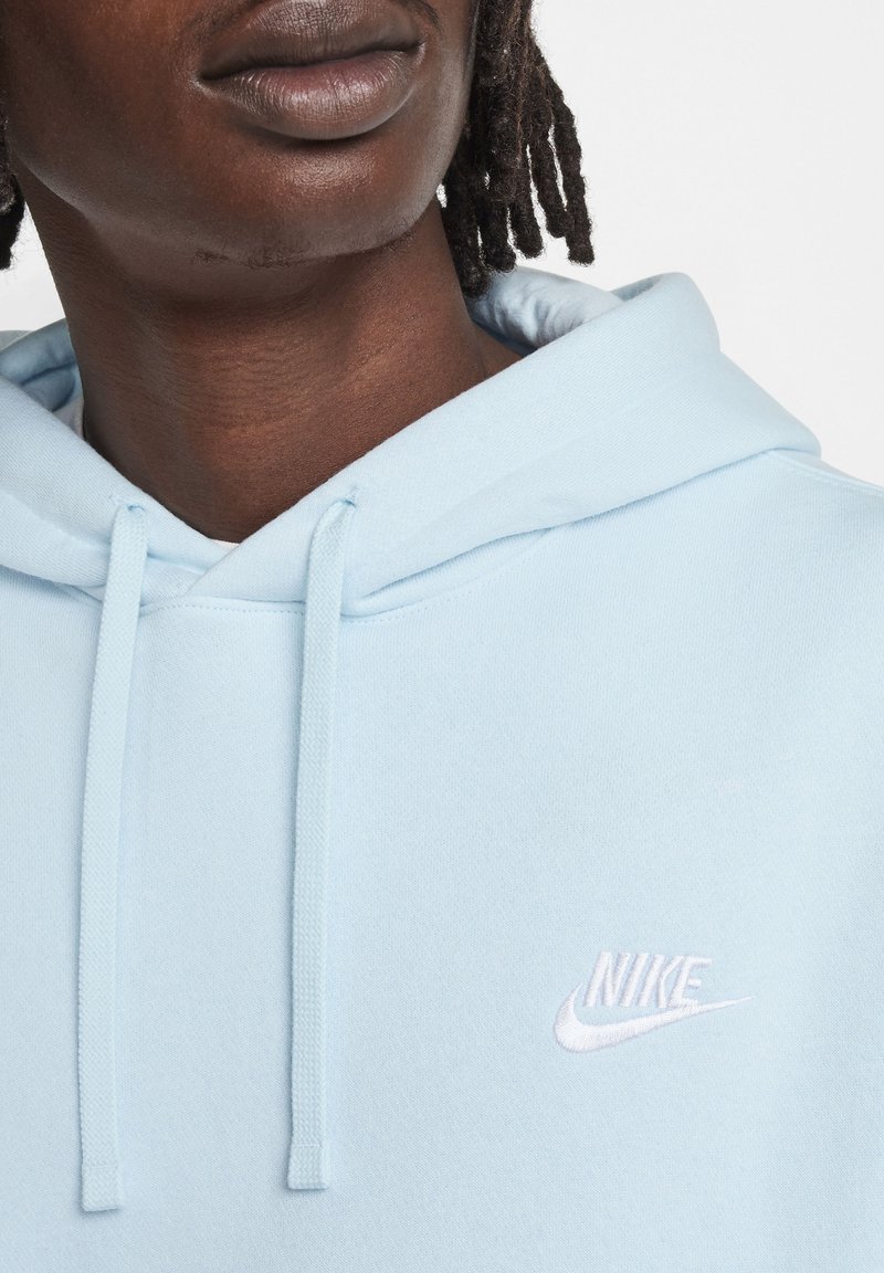 Sudadera azul clara hecha de tejido suave, con un logo de Nike bordado en blanco en el pecho y cierre con cordón en el cuello.