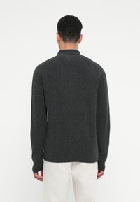 Sötétszürke kötött pulóver magas gallérral, hosszú ujjakkal és laza szabással. Texturált felület és oldalsó hasítékok az alján.