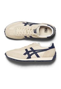 Scarpe da ginnastica beige e blu navy realizzate in camoscio e pelle, caratterizzate da un design classico, superficie testurizzata e strisce laterali a contrasto.