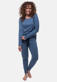 Niebieski komplet z długim rękawem i spodniami, wykonany z miękkiego materiału, o luźnym kroju i elastycznych mankietach. Spodnie mają regulowany pasek.