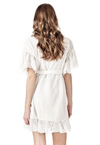 Vestido blanco con tela de ojal, mangas cortas con volantes, cinturón en la cintura y un dobladillo acampanado. La textura es ligera y aireada.