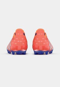 Scarpe da calcio di un rosso vivace con un colletto arancione e una suola blu. Presentano una texture liscia con accenti triangolari sul tallone.