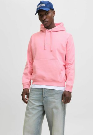 Sweat à capuche rose avec une poche avant et des cordons de serrage. Porté par-dessus une chemise blanche, associé à un pantalon en denim bleu clair.