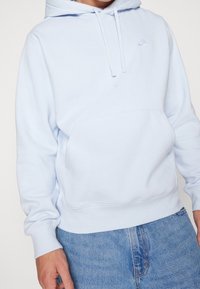 Ljusblå hoodie med ficka fram och vit Nike-logga. Tillverkad av mjukt material med ribbade muddar och nederkant.