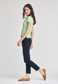 Grön kortärmad polotröja, figursydd design, matchad med mörka slim fit-byxor och tan-loafers. Enkla, rena linjer, inga mönster eller utsmyckningar.