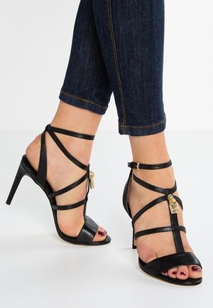 Sandales à talons hauts noires avec plusieurs fines lanières, bout ouvert et accents en métal doré. Texture en cuir lisse avec un design élégant.