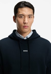 Navy hoodie featuring a drawstring hood, a front kangaroo pocket, and a white "BOSS" logo on the chest. Smooth texture and casual fit.