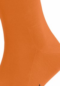 Orange Socken aus strukturiertem Stoff, mit glatter Oberfläche, nahtlosem Design und einem subtilen Logo nahe dem Bündchen.