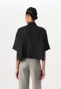 Cropped shirt nera con maniche corte e colletto strutturato, realizzata in tessuto leggero. Abbinata a pantaloni grigi aderenti con tasche posteriori.