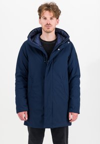 Marineblauwe pufferjas met een afneembare capuchon, vooraan drukknoopsluitingen, twee zijzakken en een contrasterende binnenvoering. Glad, gestructureerd materiaal.