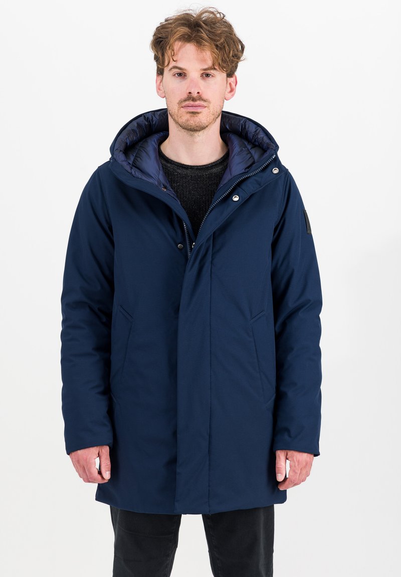 Marineblauwe pufferjas met een afneembare capuchon, vooraan drukknoopsluitingen, twee zijzakken en een contrasterende binnenvoering. Glad, gestructureerd materiaal.