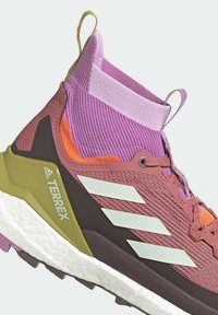 Vandre sko med høj top-design, der har en pink og brun mesh-overdel, hvide striber og en tekstureret gummisål med lilla detaljer.