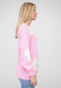 Roze gebreide trui met witte bloemmotieven, ruime pasvorm, geribde manchetten en zoom. Zachte textuur, casual ontwerp en lange mouwen.