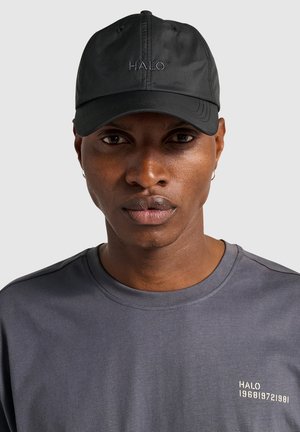 Black cap with embroidered "HALO" logo, made of lightweight material. Worn with a gray crew-neck shirt featuring subtle branding.