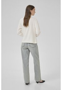 Ljuscremefärgad tröja med långa ärmar, rund halsringning och en avslappnad passform, tillsammans med högmidjade ljusblå jeans och svarta skor.