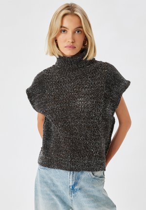 Pull en tricot à manches courtes, couleur marron foncé, avec un col cheminée. Tissu texturé avec un léger effet scintillant. Associé à un jean en denim bleu clair.