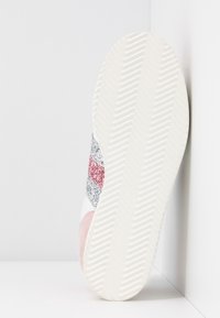 Vita sneakers med rosa, silver och röda glittrande ränder på ovandelen. Den texturerade sulan har ett fiskbensmönster för bra grepp.