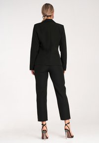 Czarna, dopasowana marynarka i przylegające spodnie, obie o gładkiej fakturze. Slim-fit, z długimi rękawami i prostymi nogawkami.
