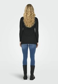 Black ribbed long-sleeve top, blue skinny jeans, black knee-high boots, wavy long hair, viewed from behind against a plain background.