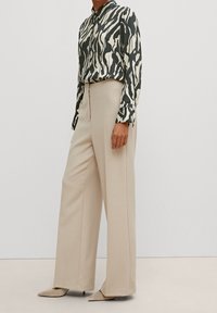 Long beige trousers paired with a black and white striped button-up shirt, featuring a collar and cuffed sleeves. Smooth fabric texture.