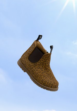 Bottine à enfiler marron imprimé guépard avec panneaux latéraux élastiques noirs et languettes, montrée flottant devant un ciel bleu clair.