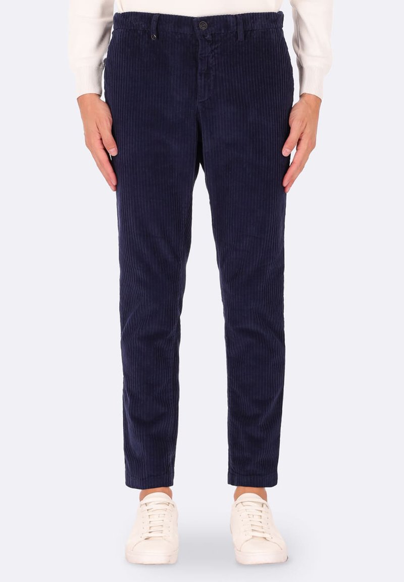 Pantaloni in velluto a coste blu navy con una vestibilità slim, caratterizzati da motivi a righe verticali, tasche frontali e chiusura con bottone, abbinati a sneakers bianche.